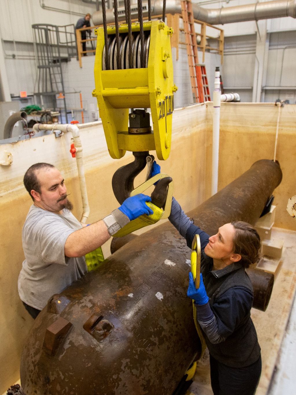 Conservators wrapping a belt around USS Monitor's Dahlgren gun to lift it out of its tank.
