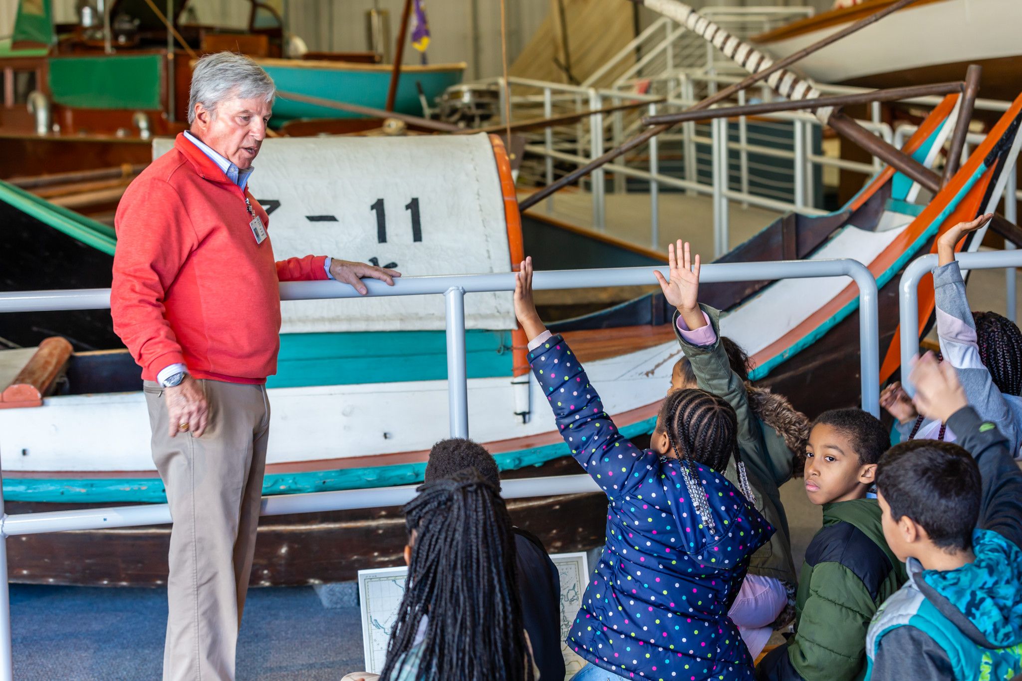 Docent seen teaching children in the International Small Craft Center. Multiple students are seen raising their hands and engaging with the program.