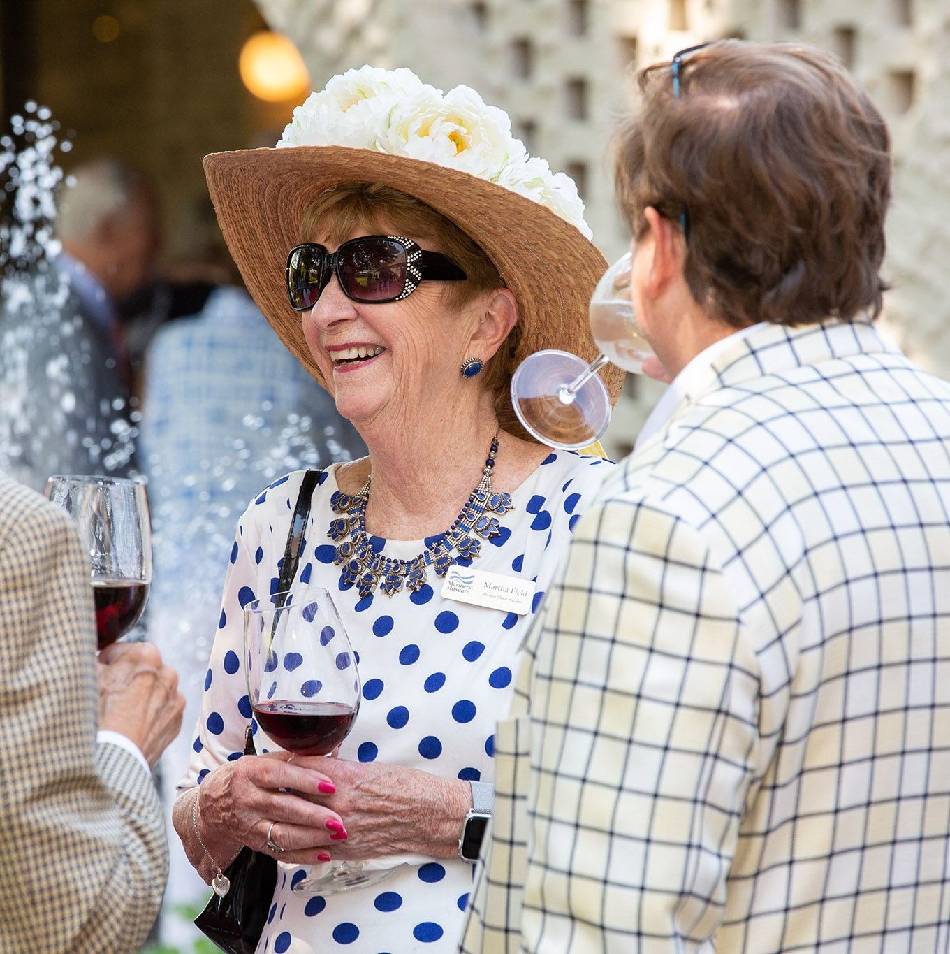 Martha Field standing outside in the Mariners' South Courtyard enjoying a glass of wine with other Bronze Door members. 