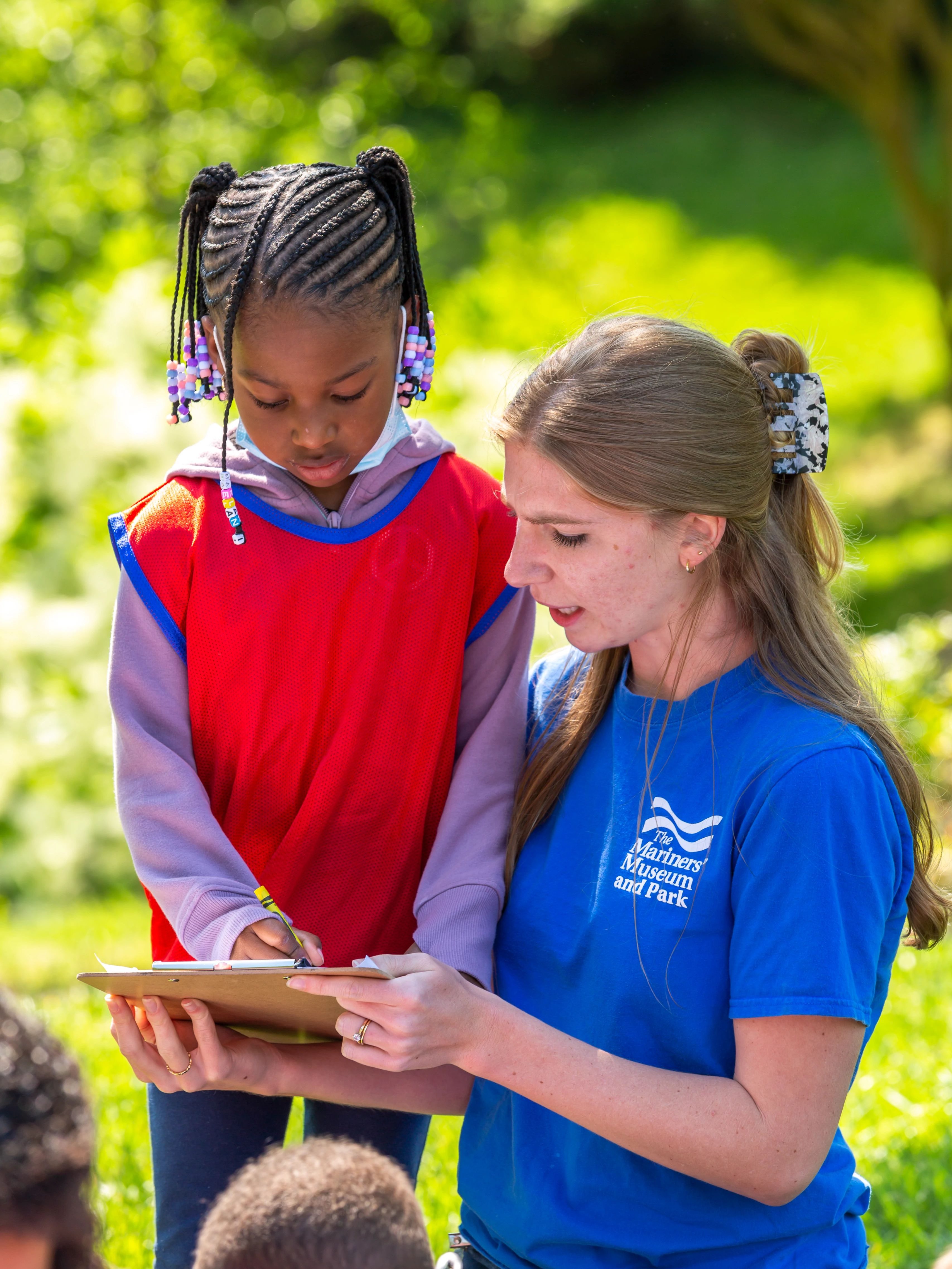 Mariners' Education team member kneeling beside a cute little girl. They're working together on an educational enrichment program in the Park.