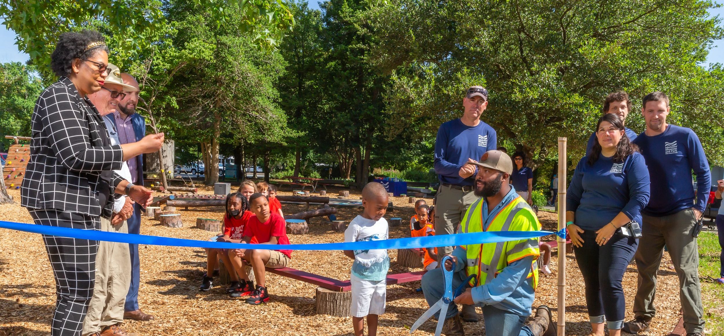 Ribbon cutting ceremony for the new Lil' Mariners" Play Zone. A group of kids are sitting on benches while the Museum's team and strategic partners stand near.