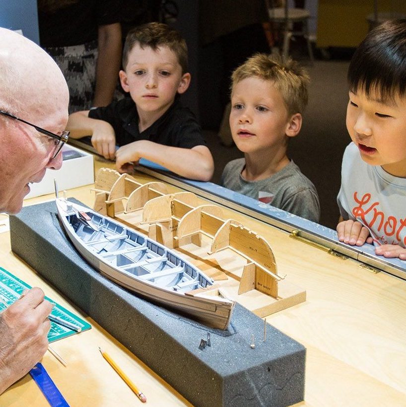 three children look at a ship model while talking to a modelmaker. 
