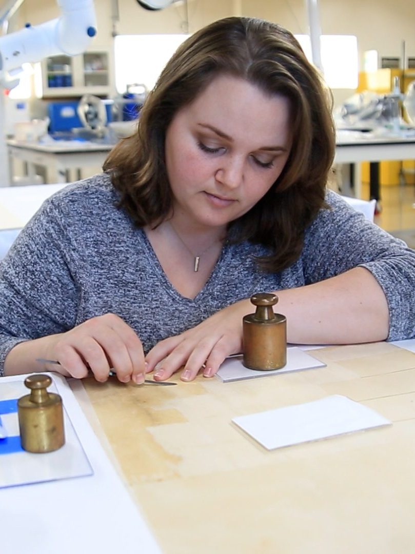Paper Conservator Lindsey Zachman is carefully removing a harmful backing board from a watercolor to help preserve the original paper.