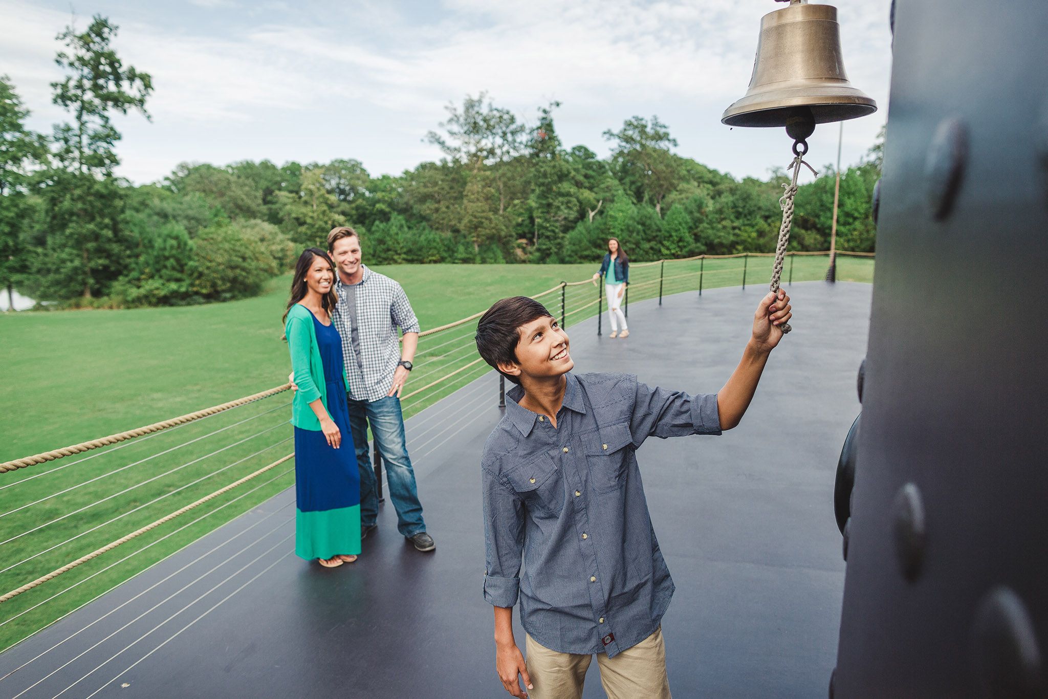 Family standing on the USS Monitor replica, with a teenage boy ringing Monitor's bell.