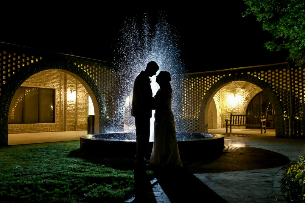 Silhouette of a couple standing in front of a fountain.