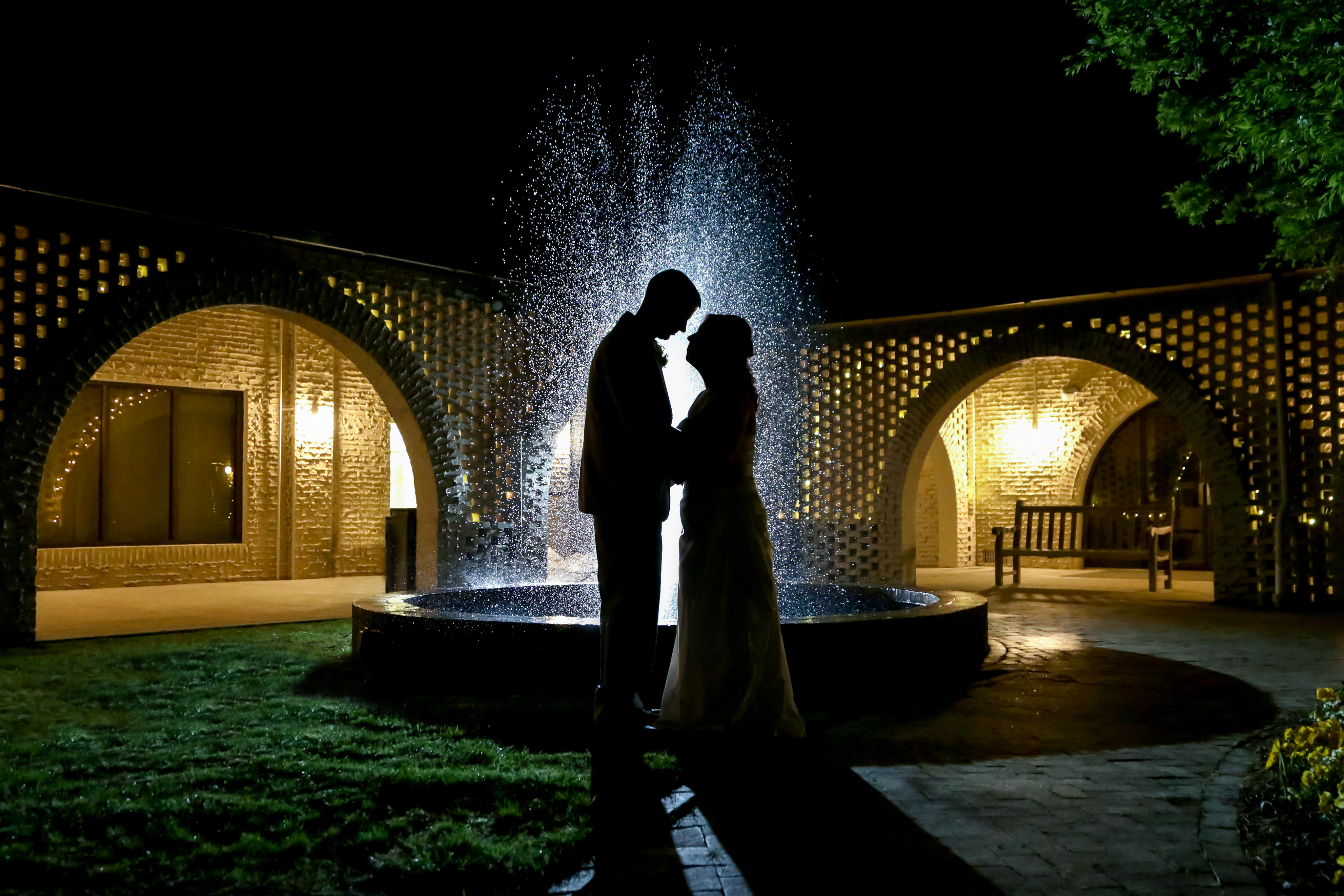 Silhouette of a couple standing in front of a fountain.