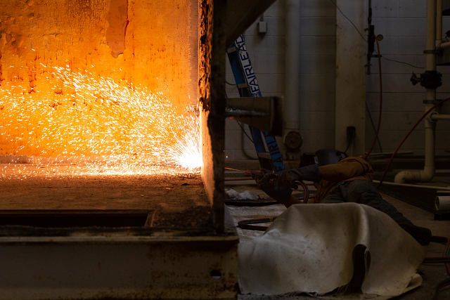 A welder from Fairlead works to cut through the outer wall of the former USS Monitor Condenser Tank in the Batten Conservation Complex.