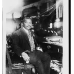 Portrait of Marcus Garvey sitting in a chair near a desk.