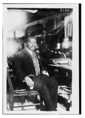 Portrait of Marcus Garvey sitting in a chair near a desk.