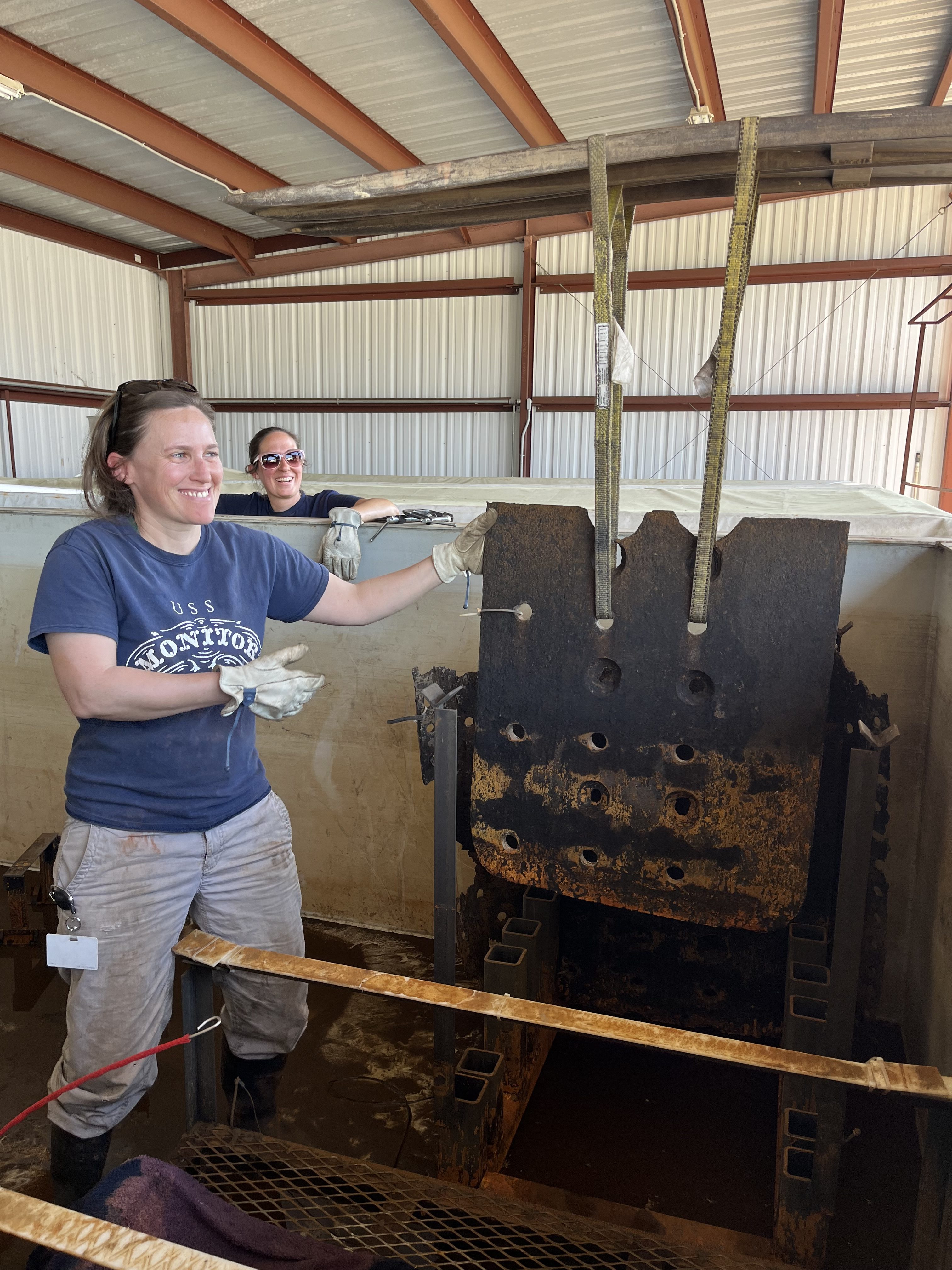 Senior Conservator Elsa Sangouard and Archaeological Conservator Lesley Haines making sure an object (accession number MNMS-2002-001-1885T) is lowered into the correct spot in the tank.