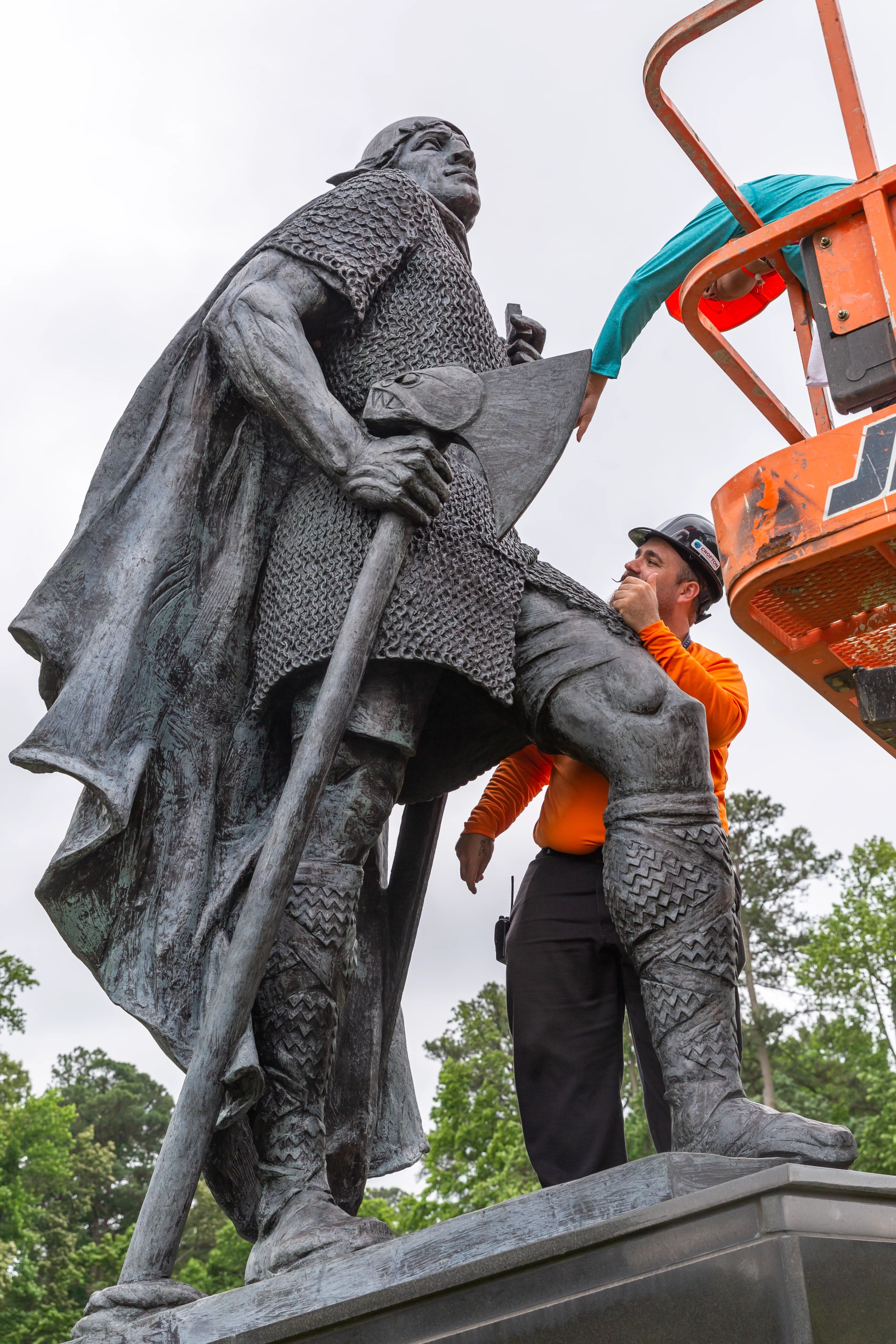 Image of Senior Objects Conservator Erik Farrell on the Leifr sculpture’s base and Conservation intern Marimar Bracero Rodríguez on an orange lift examining and documenting areas of the statue.