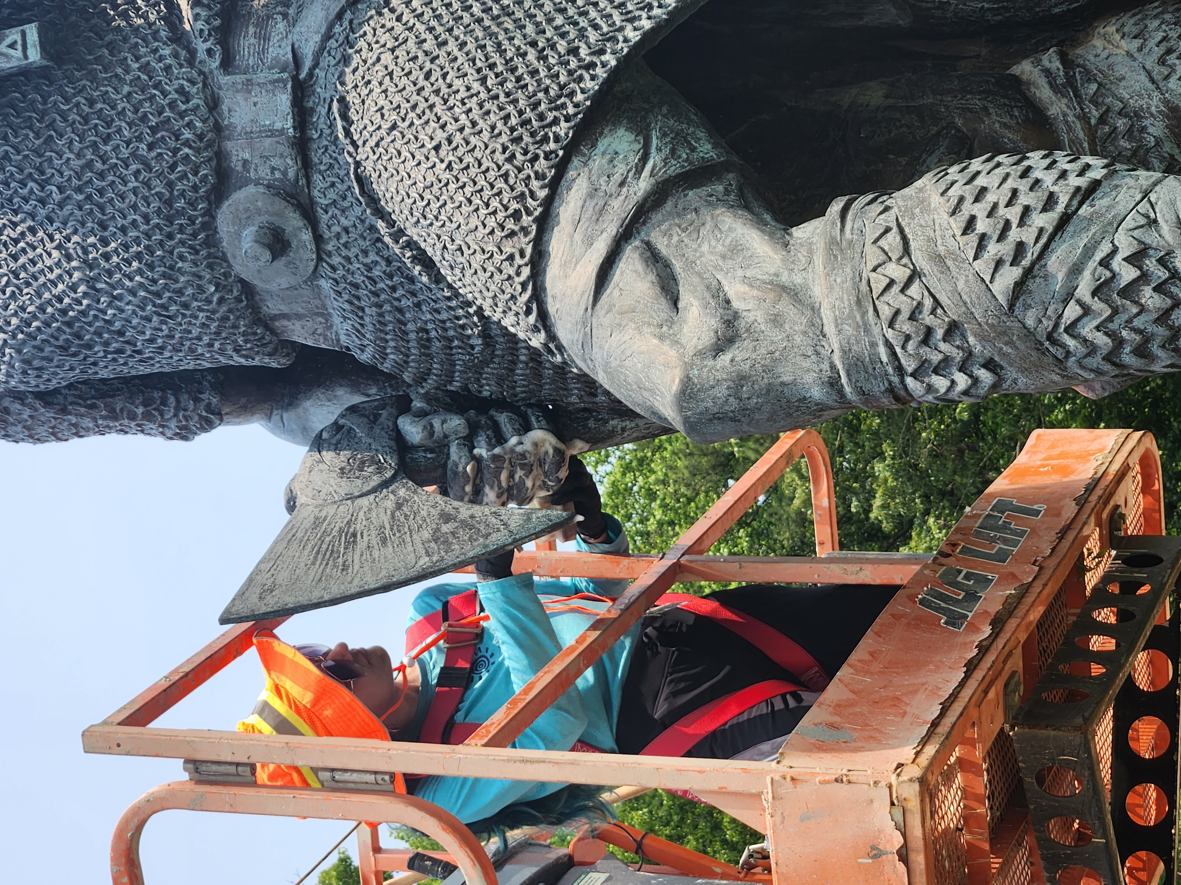Image of Conservation intern Marimar Bracero Rodríguez on an orange lift cleaning the hand and axe of the statue of Leifr Eiriksson.