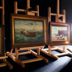 4 paintings sitting on easels in a dark studio lit only by a back light.