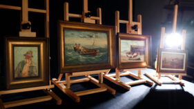 4 paintings sitting on easels in a dark studio lit only by a back light.