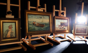 4 paintings sitting on easels in a dark studio lit only by a back light.