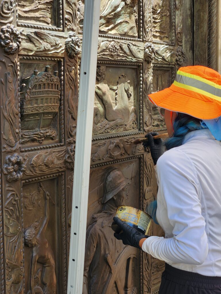 Image of Intern Marimar applying colored wax with a brush to a door.