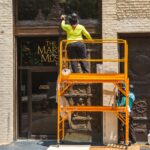 Image of Senior Objects Conservator Erik Farrell on a scaffold cleaning the top panel and Intern Marimar cleaning a door.