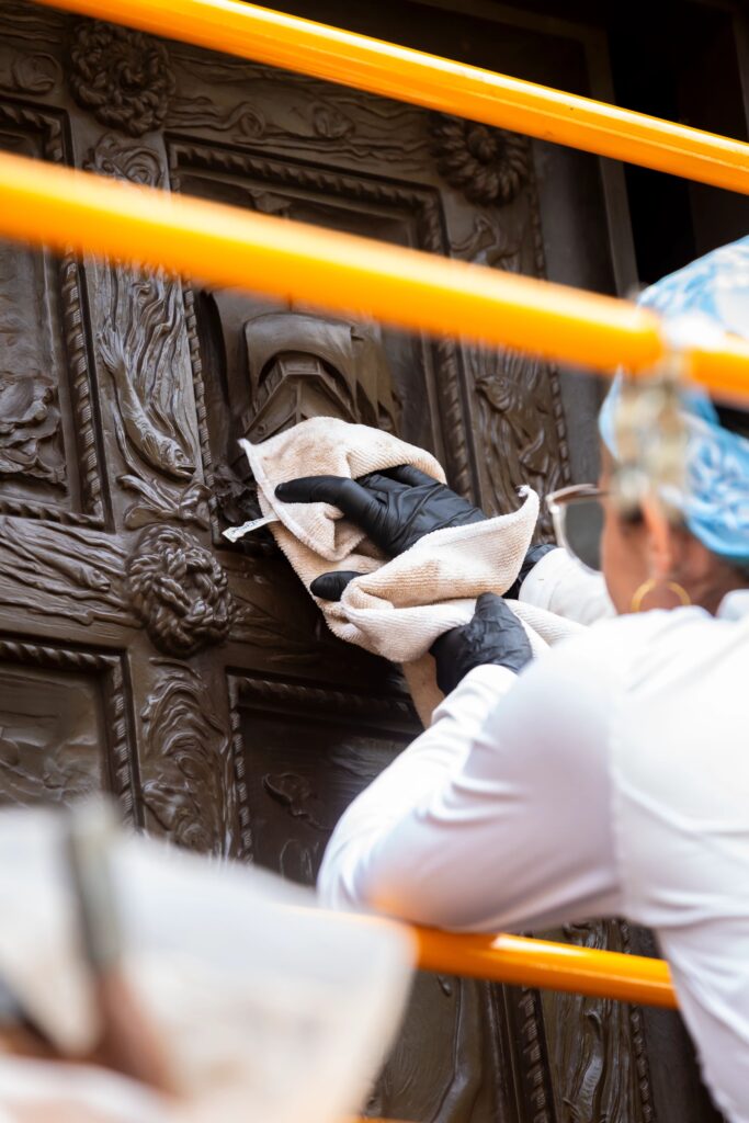 Image of Intern Marimar on a scaffold using a cloth to buff the door.