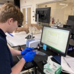Image of Conservation intern Harrison Biggs working with the ATR-FTIR. He is removing a sample from a plastic bag.
