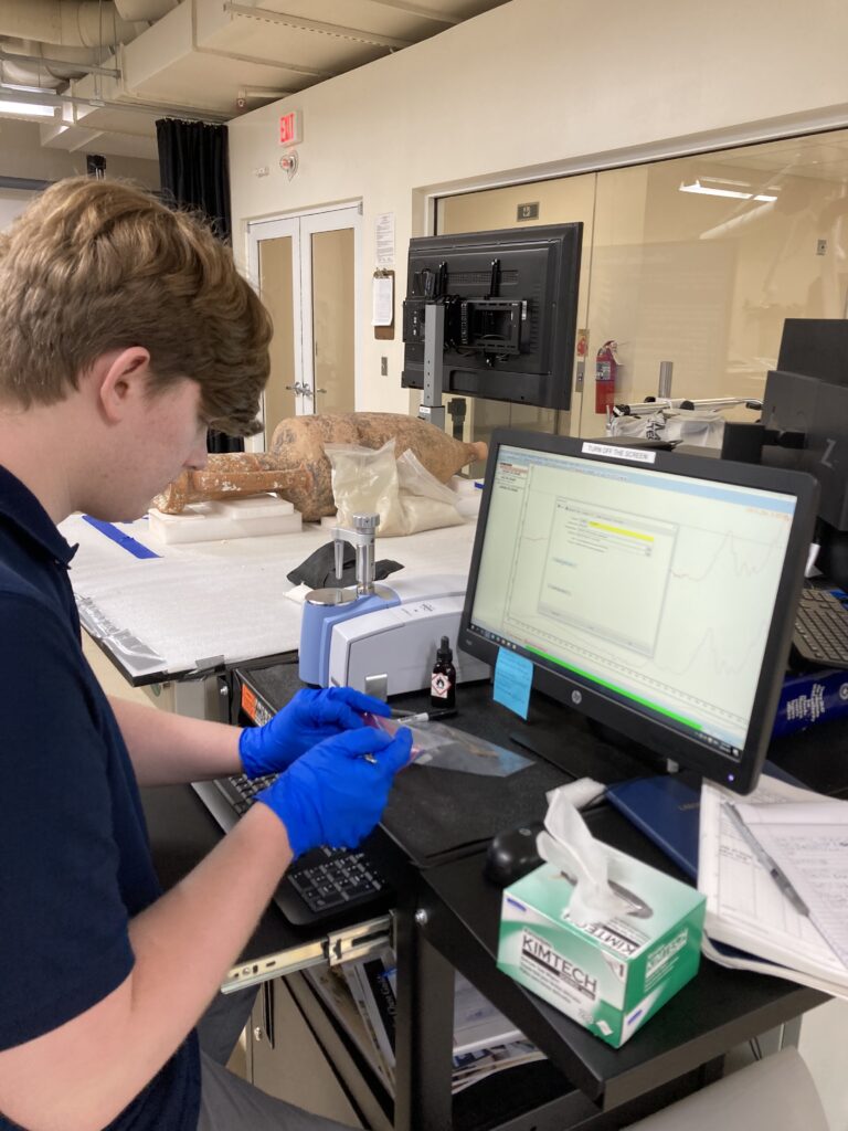 Image of Conservation intern Harrison Biggs working with the ATR-FTIR. He is removing a sample from a plastic bag.