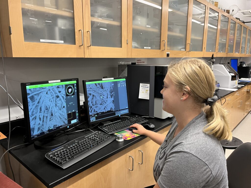 Photo of scientist looking at computer screens with black and white fibrous images.