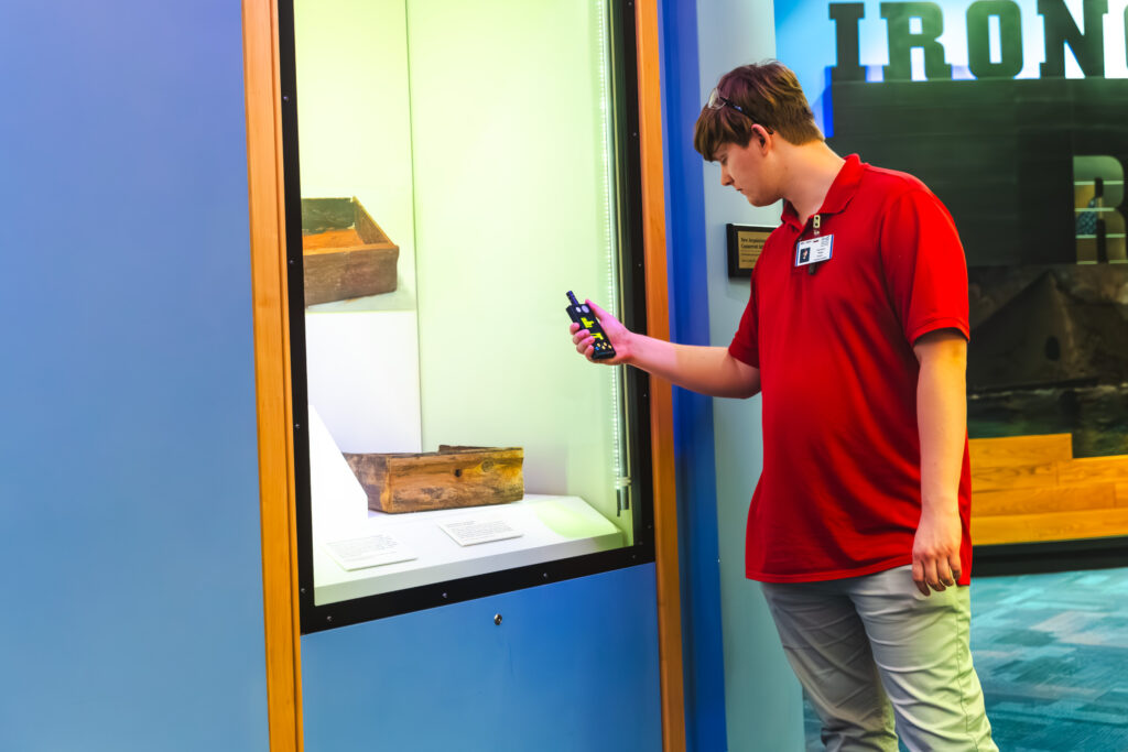 Image of Conservation intern Harrison Biggs holding a light meter up to a display case.