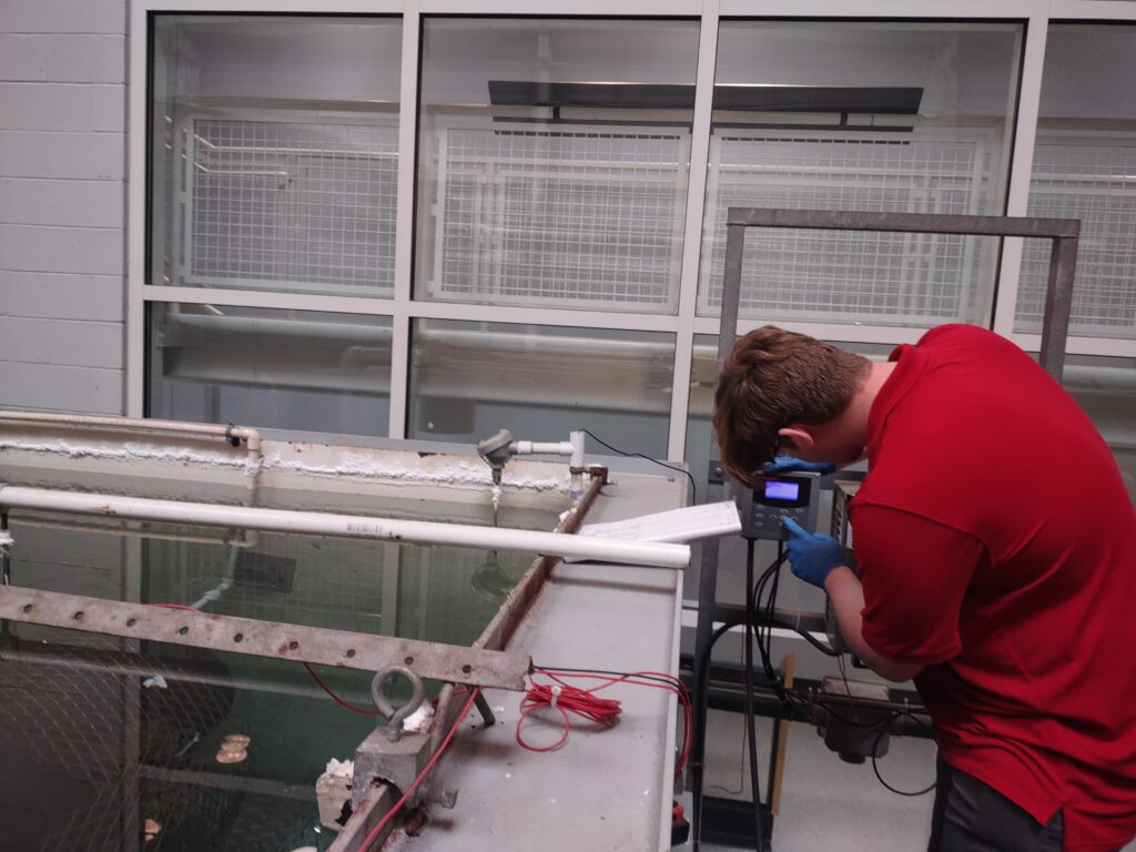 Image of Conservation intern Harrison Biggs operating a small keypad next to a large tank holding one of the Monitor’s guns.