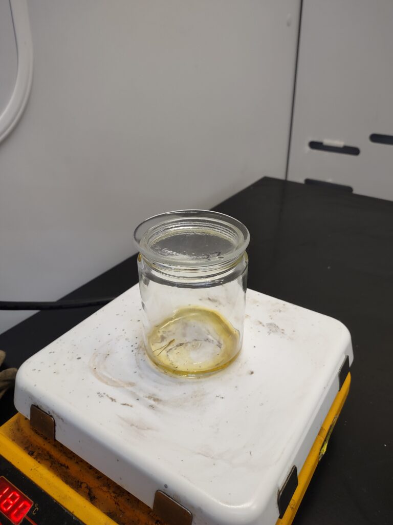Image of a jar filled with melted resin sitting on a white hotplate. The resin is bright yellow in color.