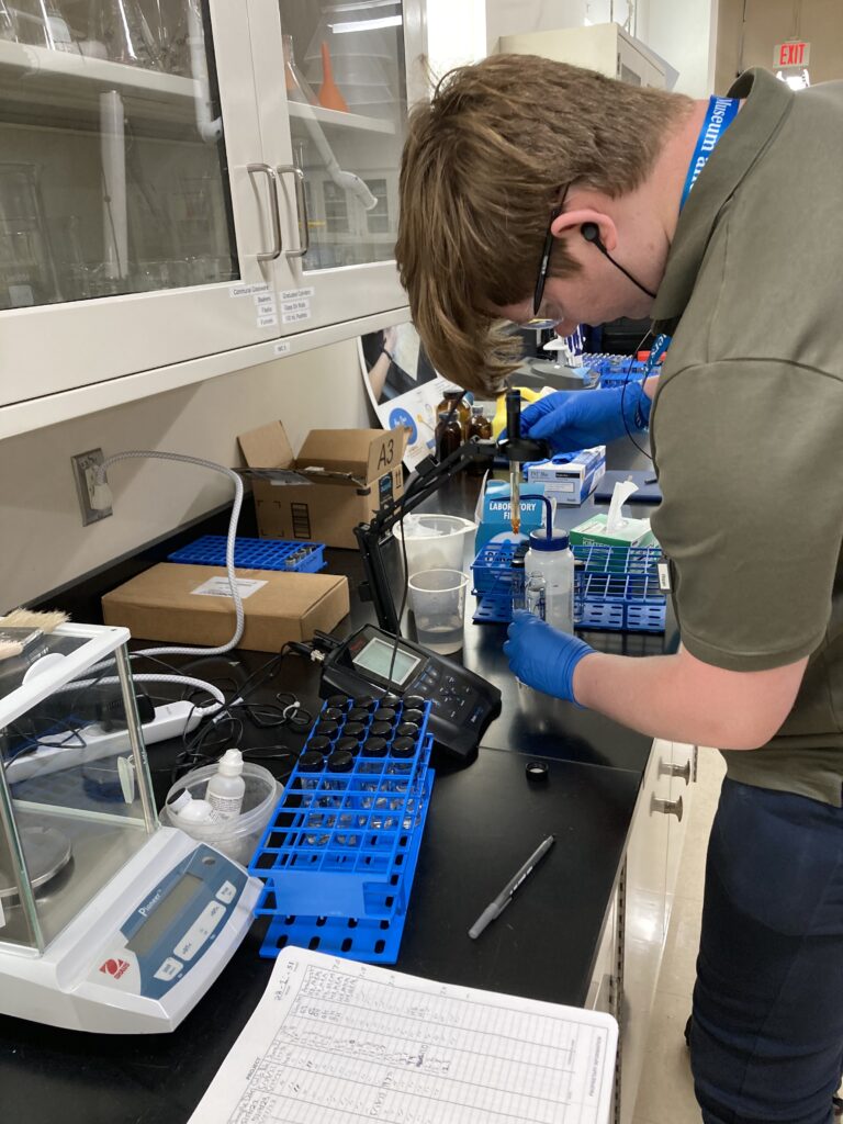 Image of Conservation intern Harrison Biggs working with a pH probe, measuring the pH of treatment solution samples.