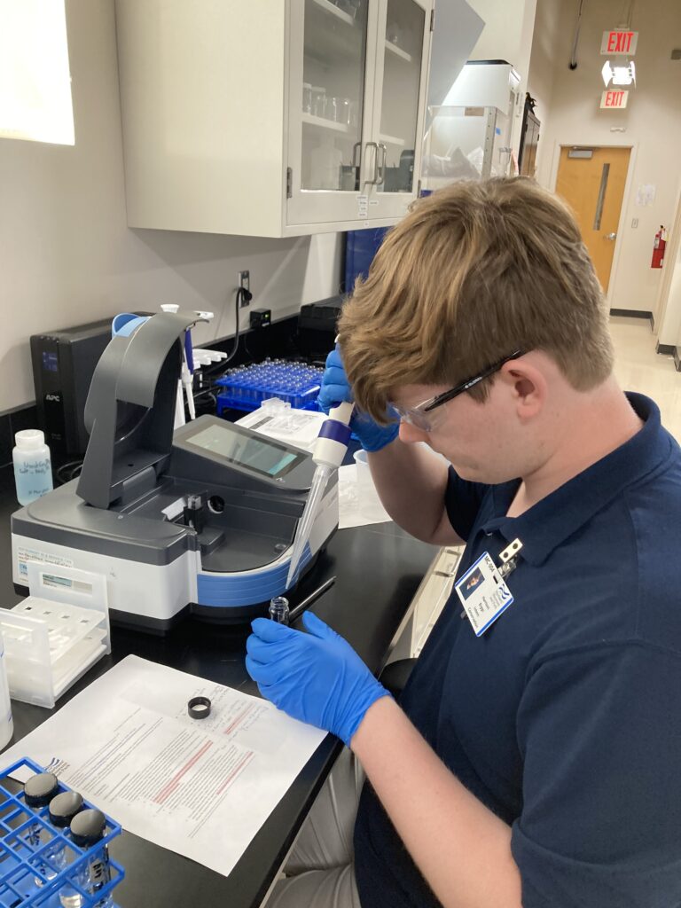 Image of Conservation intern Harrison Biggs working with the UV-Vis spectrophotometer. He is using a micropipette to prepare a sample in a glass vile.