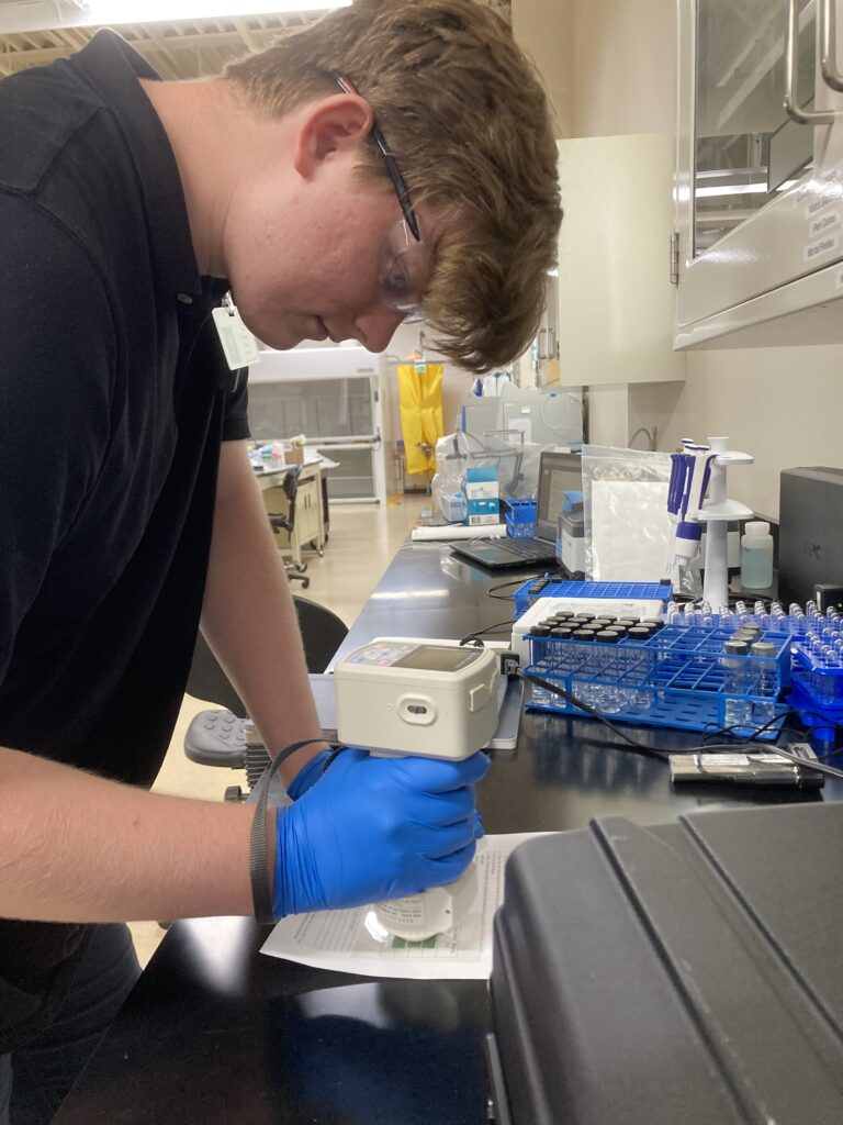 Image of Conservation intern Harrison Biggs holding a colorimeter up to a colored slip attached to a piece of paper.