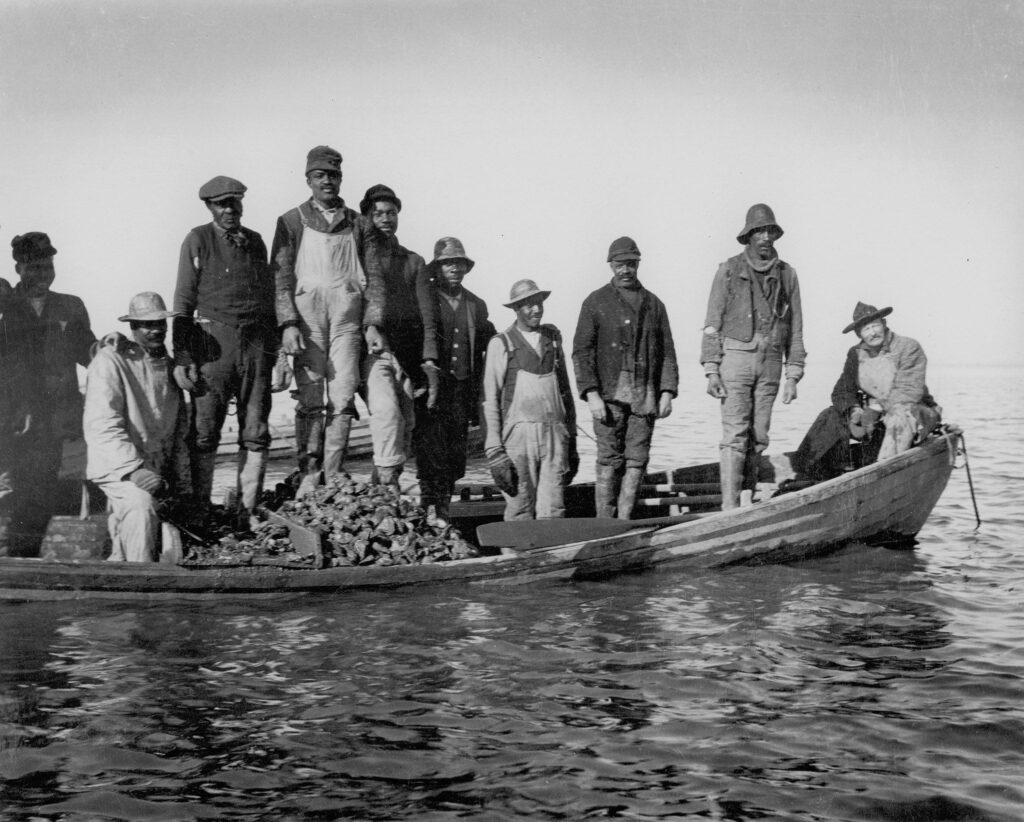 Ten men pose for a photograph in a rowboat which is loaded with oysters on York River.
