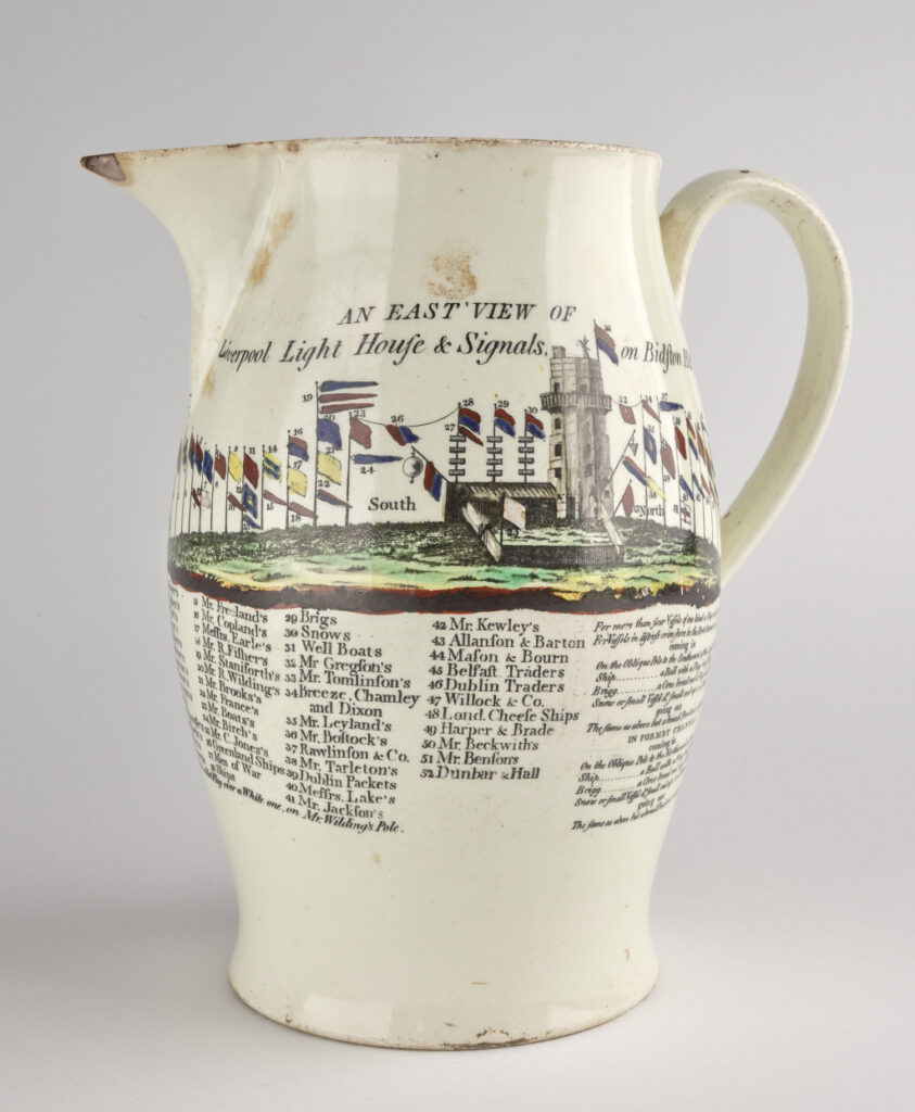 An antique white jug with a colorful print of a lighthouse and flags