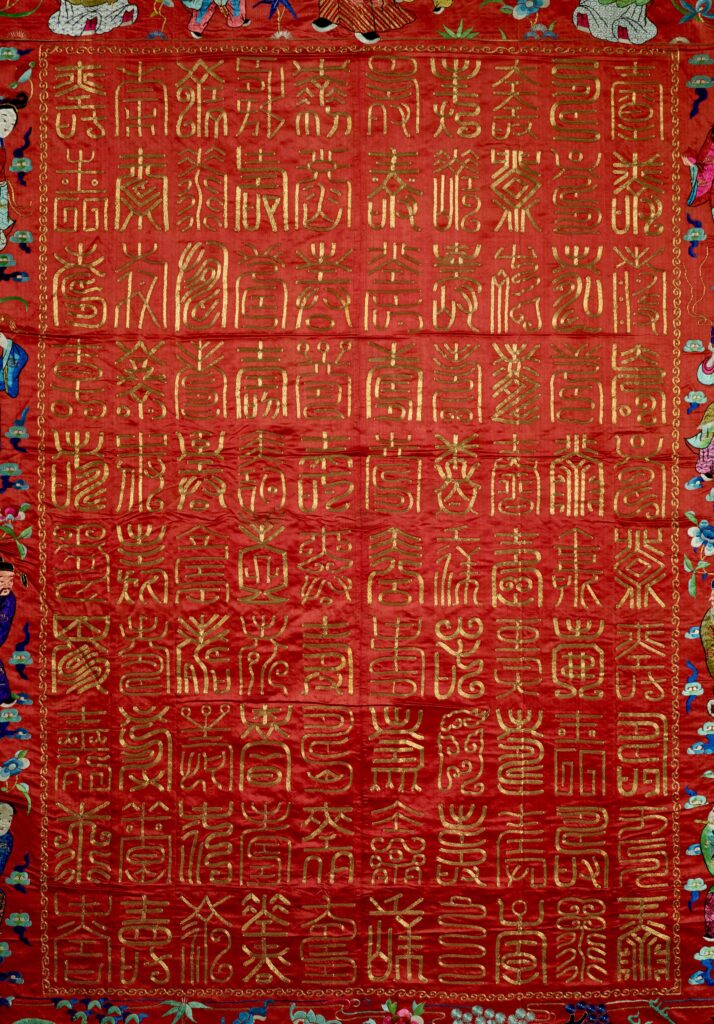 Chinese writing in gold thread forms a neat rectangle in the tapestry's center.