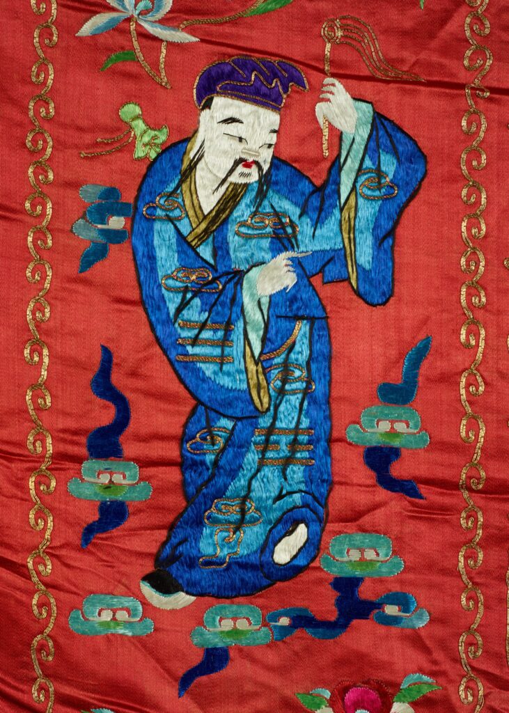 On the tapestry, a figure of a god dressed in blue carries a fly-whisk in his hand.
