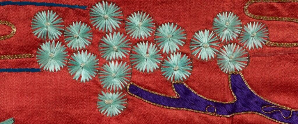 On the tapestry, a branch holds several blue flowers outlined by faint black marks.