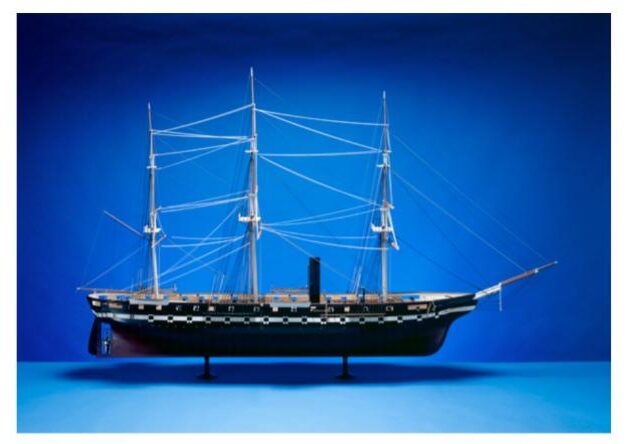 A model of a ship stands against a blue background.