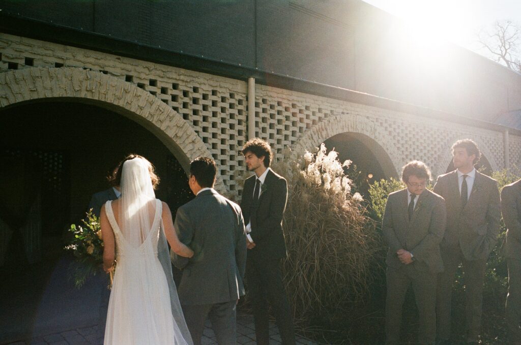 A bride and groom stand at an alter while groomsmen watch.