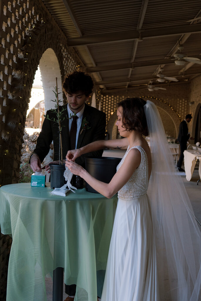 A bride and groom retrieve gloves. Plants are on the table.