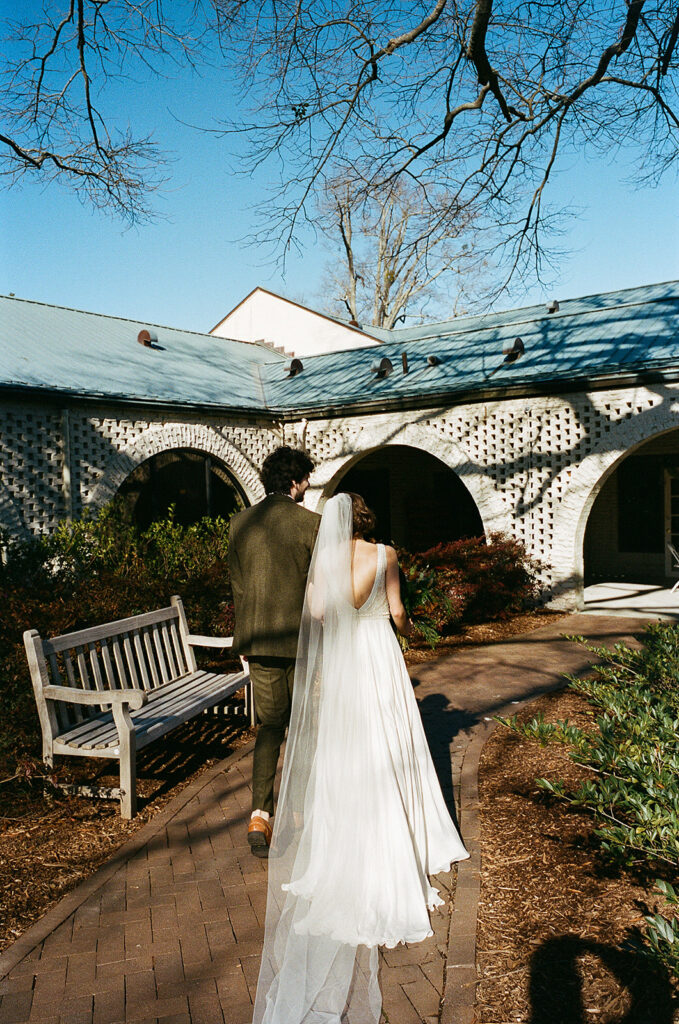 A bride and groom walk down a pathway in a courtyard.