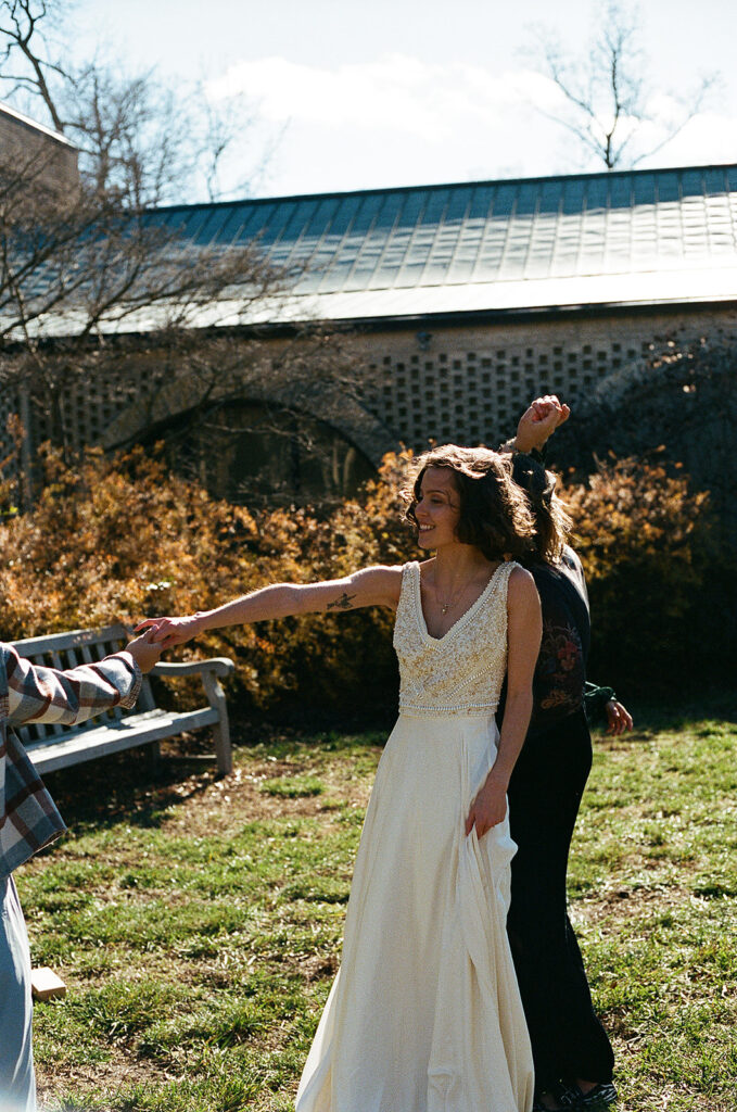 A bride dances in a courtyard, holding the hand of someone off camera