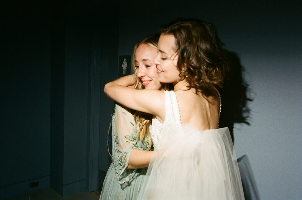 Two women embrace. One is wearing a wedding dress.