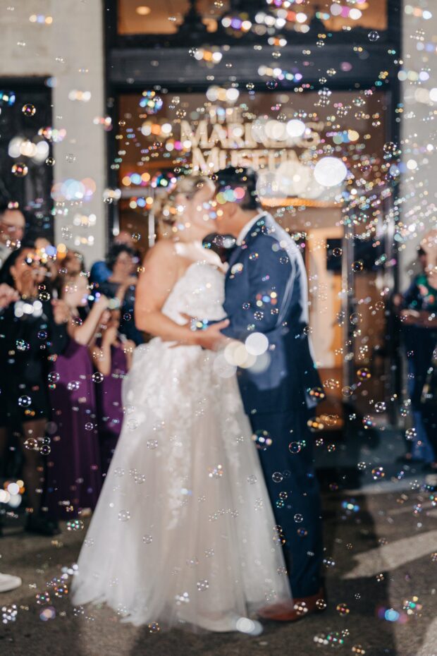 Bride and groom kissing while surrounded by bubbles.