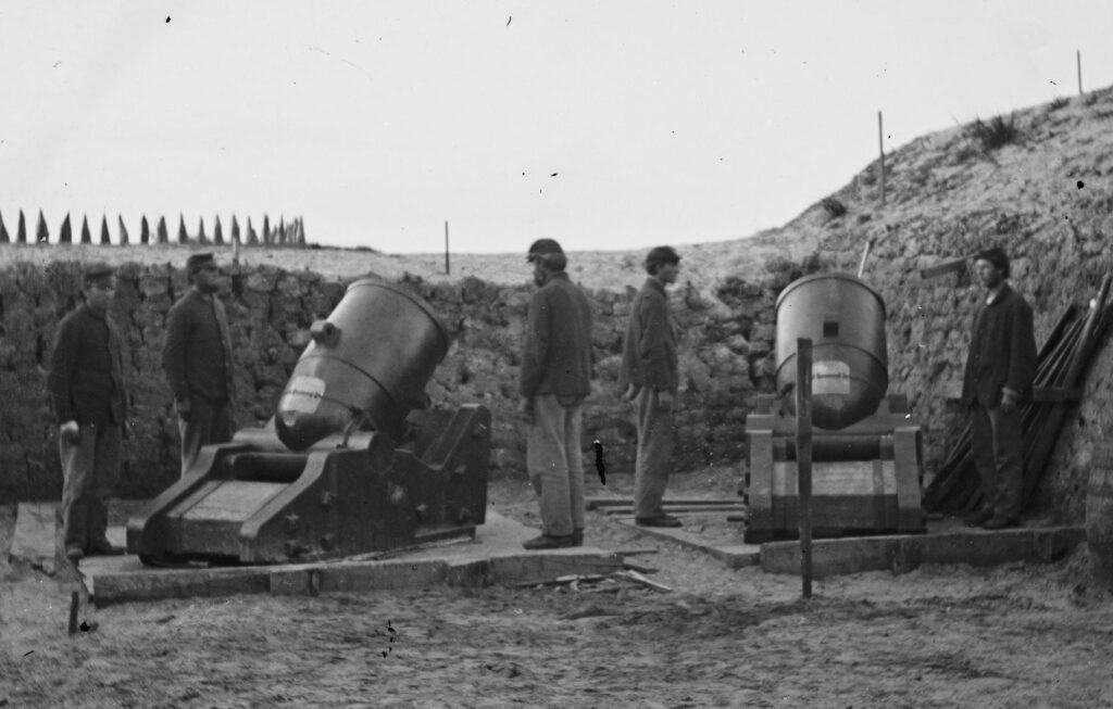 Black and white image of five soldiers surrounding two 10 inch Seacoast Mortars on Morris Island.