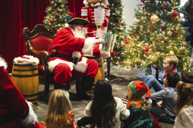 Santa wears a pirate hat while reading a story book to children.