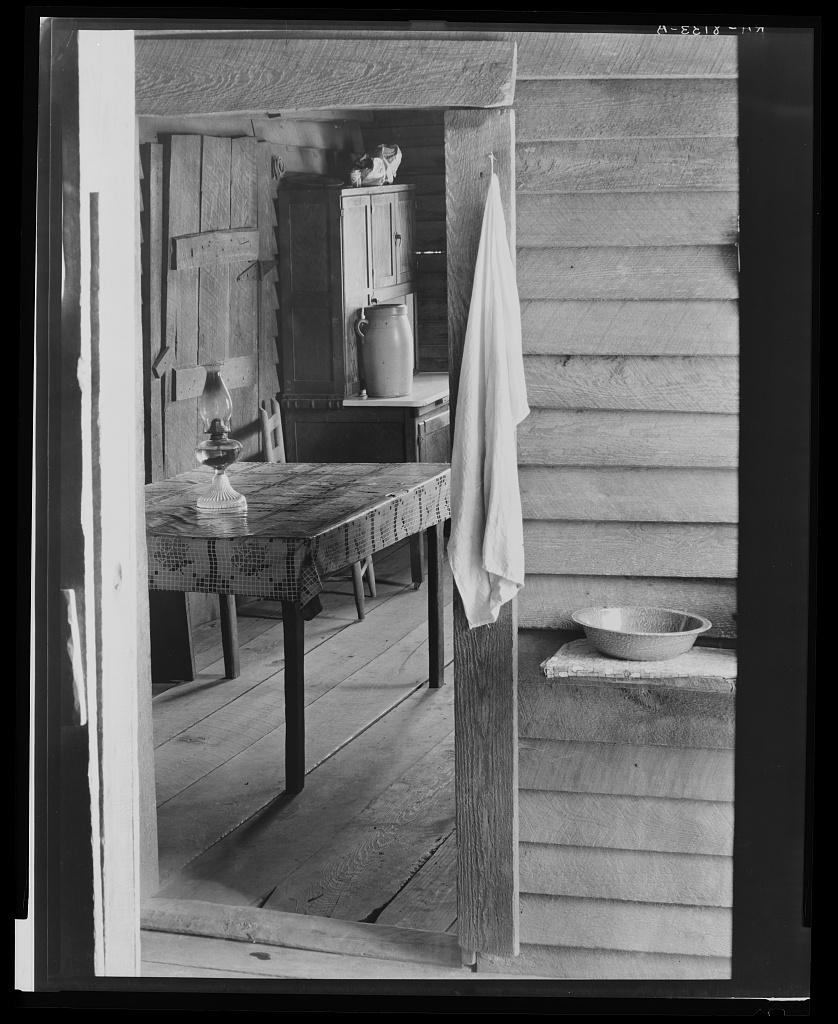 black and white photo of a door frame that looks into a room with an oil lamp on a table and other furnishings
