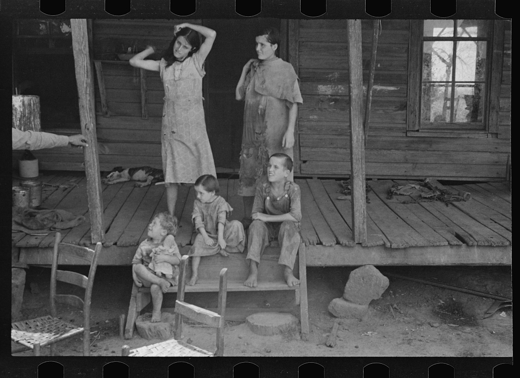 a black and white photo of 5 children in worn clothes on an aging porch