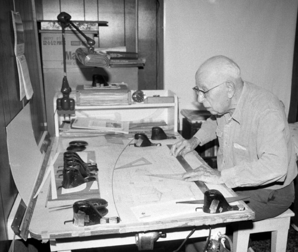 black and white photo of a man with glasses holding a measurement tool while sitting at a table