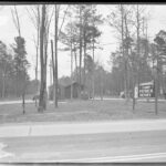 black and white photo of a building behind trees with the sign "Camp Patrick Henry" by the road