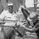 black and white picture of 2 men. One is holding a level and the other is holding a measurement tool in front of the level